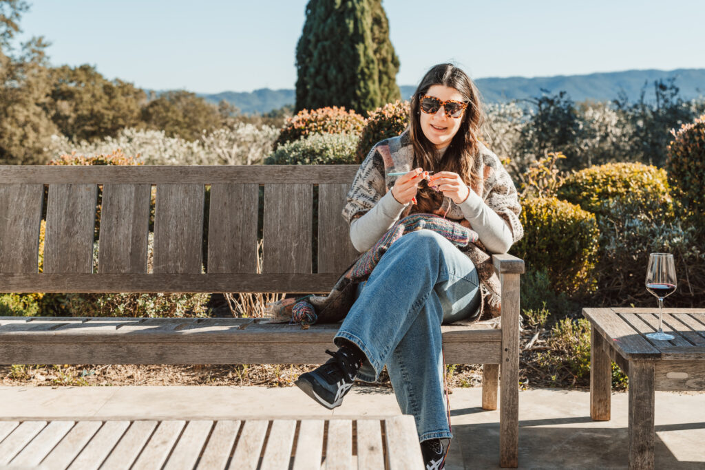 A woman sitting on a bench outside knitting.