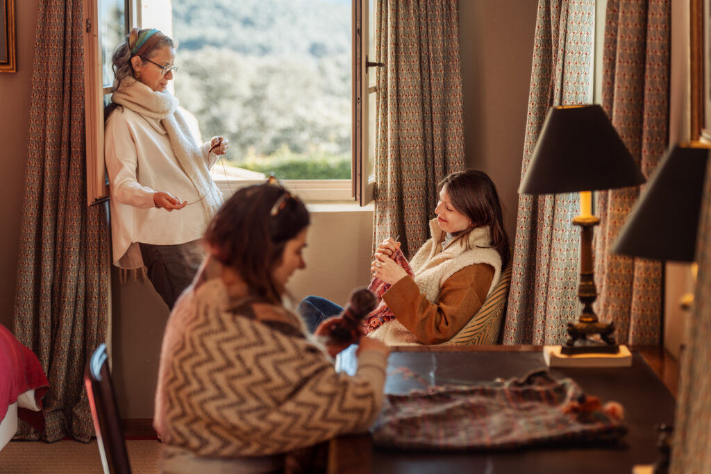 Several women all knitting in the same room spread out around the room.